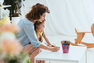selective focus of nanny and child drawing with pencils together