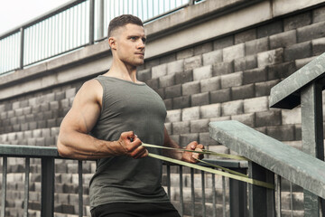 Muscular man during workout with a resistance rubber band on a street.