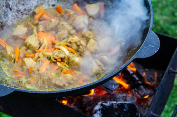 Cooking food on an open fire in a cauldron. Meat with vegetables is fried in a metal wok