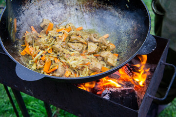 Cooking food on an open fire in a cauldron. Meat with vegetables is fried in a metal wok