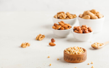 A handful of pine nuts in a wooden bowl, assorted nuts on a light background. Healthy snacks, healthy fats. Copy space.