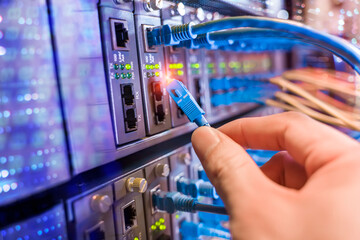 man working in network server room with fiber optic hub for digital communications and internet