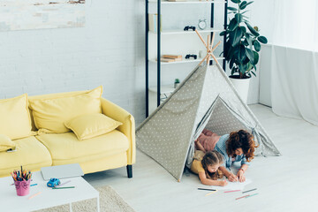 high angle view of young nanny and child drawing together while lying in kids wigwam