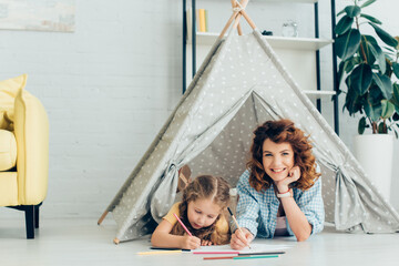 happy nanny looking at camera while drawing together with cute child in kids wigwam © LIGHTFIELD STUDIOS
