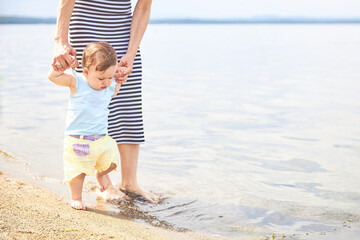 Fototapeta na wymiar Mom learns to walk little baby on the sand at the beach