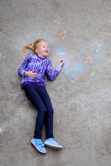 Fototapeta premium Happy little girl have fun introducing herself to the singer profession. The concept of dreaming about a future profession. The child lies on the ground, top view. Childhood and dreams concept.