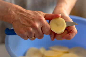 Fresh tasty potatoes cut into perfect round slices. Woman sliced potatoes in round shape with knife in a blue bowl.