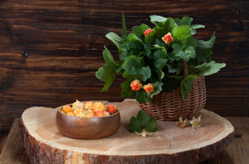 Cloudberries in a basket and a wooden bowl on a cut tree