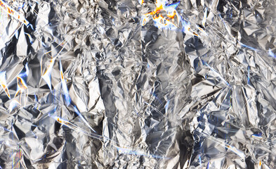 Metallic abstract background. Wrinkled texture. Shiny silver crinkled foil with orange blue gleam.