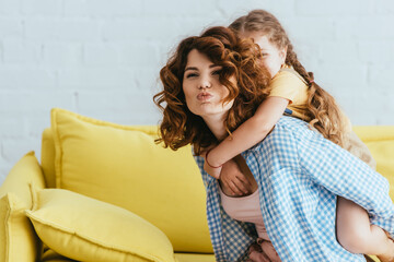 young nanny making duck face while piggybacking kid at home