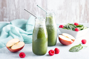 Two glass bottles of green smoothie with spinach, raspberry and apple on concrete table, still...