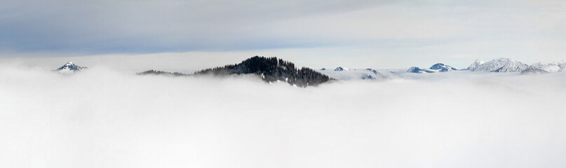 Winter Panoramic View to snow covered mountains above the clouds of inversion fog. View from Riedberger Horn in Allgau, Bavaria, Germany.