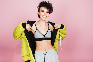 Beautiful teenager girl sincerely smiles and laughs in sports stylish clothes in the studio on a pink background. Bright girl with a short flying hairstyle in a puffed neon lemon jacket 