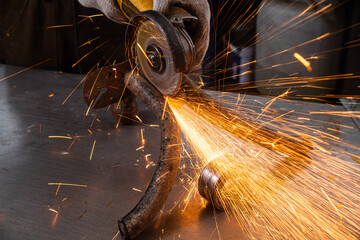 Close-up on the sides fly bright sparks from the angle grinder machine. A young male welder in a...