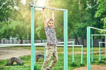 Strong kid doing pull ups on sports ground