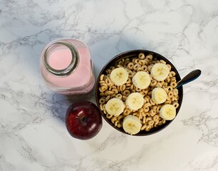 Looking down at bowl of cereal with banana slices, red apple, and pink milk