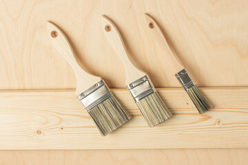New paint brushes on unpainted pine board on wooden background. Home renovation or DIY concept. Top view.