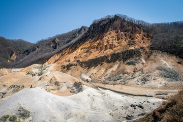 Beautiful view of Noboribetsu Jigokudani or Hell Valley in sunny day with blue sky in background. Autumn season and sulfur gas steaming out from ground.