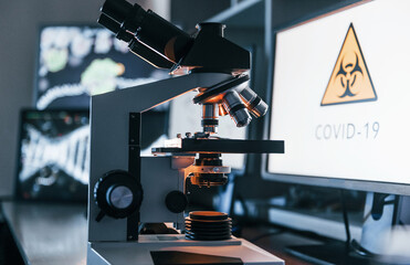 Close up view of modern microscope indoors in lab with monitors. Conception of coronavirus