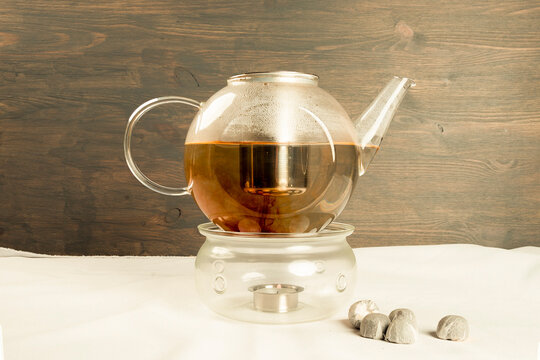 Teapot with candle warmer and mini tuo chai tea. In studio with white and wooden background. The reddish color of the tea and the setting is ideal for backgrounds and advertising.