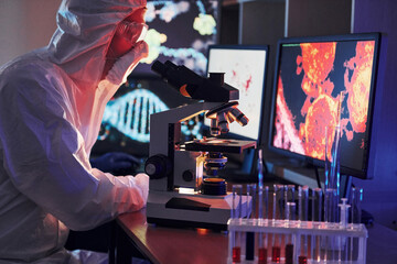 Monitors with information on the table. Scientist in white protective uniform works with coronavirus and blood tubes in laboratory