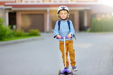 Little boy in safety helmet riding scooter to school. Quality protect equipments for safety kids on street of city. Back to school concept.