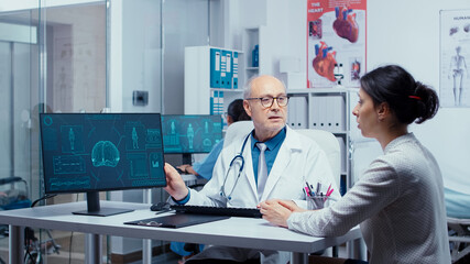 Old experienced practitioner presenting modern X Ray on computer display to young patient. Practitioner explayning medicine computer diagnosis image X Ray. Radiology health care scan analyzing in