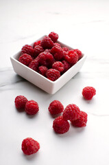 Vertical image. White bowl full of rasberries on the white marble table