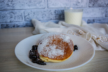 pancakes with berries and powdered sugar on a white plate and a glass of milk
