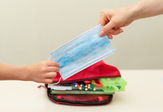 Back to school. Education concept. Collect your backpack for school. A child puts a protective medical mask and an antibacterial hand cleaning gel (manual alcohol) into aknapsack on light background. - Powered by Adobe