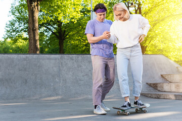 Carefree teenager couple in a skate-park. Guy giving a lesson of skateboarding for his girlfriend.