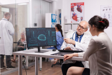 Senior doctor pointing at ct scan on computer in hospital office for young patient. Young medic...