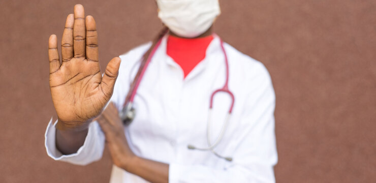 coronavirus stop concept. African American girl doctor, in a protective mask, white coat, shows her hand to stop the coronavirus infection, covid 19-20.