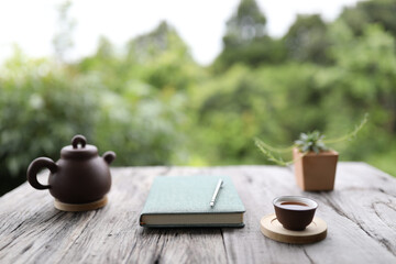 Brown traditional teapot and cup with green notebook on rustic grey wooden table