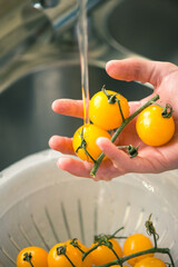 Human hand washing yellow cherry tomatoes under running water