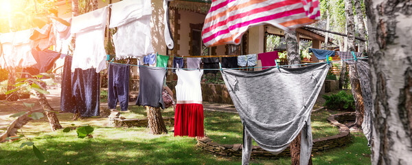 Domestic real life scene of many children and adult fresh clean washed clothes hanged on birch tree clothesline with pins. Home yard on bright sunny summer day outdoors. Lifestyle backyard garden