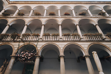 Old Renaissance three-story arcade, roses and other flowers in hanging pots on the balconies. Ancient architecture of Lviv, Ukraine. View of the patio from below. © shchus