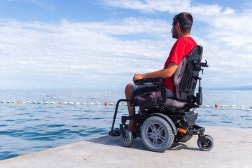Naklejka premium Man sitting in a wheelchair on the beach. Dangers of jumping into water from heights. Head and spine injury.