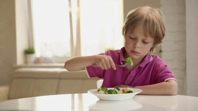 Boy tries to eat a vegetables but dosen't like it and rejects the food. Healthy food concept. Children and vegetables