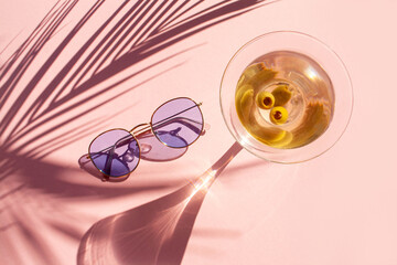 Martini glass, sunglasses and palm leaf shadow on pink background