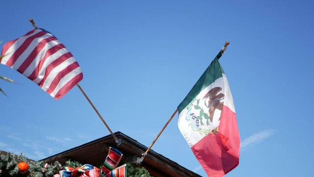 Mexican tricolor and American flag waving on wind. Two national icons of Mexico and United States against sky, San Diego, California, USA. Political symbol of border, relationship and togetherness.
