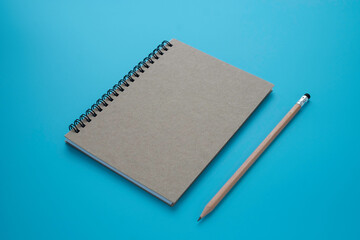 Top view above of brown spiral notebook and pencil isolated on blue background for design a mockup. 