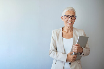 Portrait of a beautiful elderly business woman, smiling, isolated on grey background. Woman headshot looking at camera. Portrait of beautiful mature woman. Smiling senior woman.