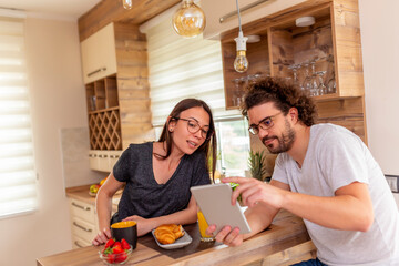 Couple surfing the Internet using tablet computer and eating breakfast