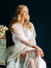 Morning of the bride. Beautiful girl in a white coat sitting in front of the window.