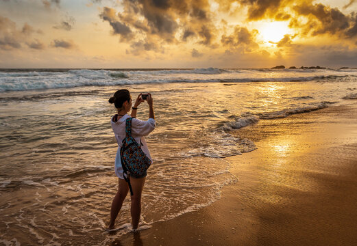 girl takes pictures of the sunset on the beach with a smartphone