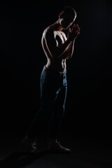 Fototapeta na wymiar Silhouette picture of a hot shirtless muscular man posing in jeans in a dark studio.