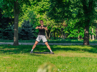 A young man practices yoga with the variations of the goddess pose outdoor in the park