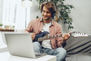Man playing electric guitar and recording music into laptop