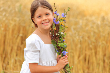 Little girl with a bouquet of wildflowers in her hands in a wheat field.